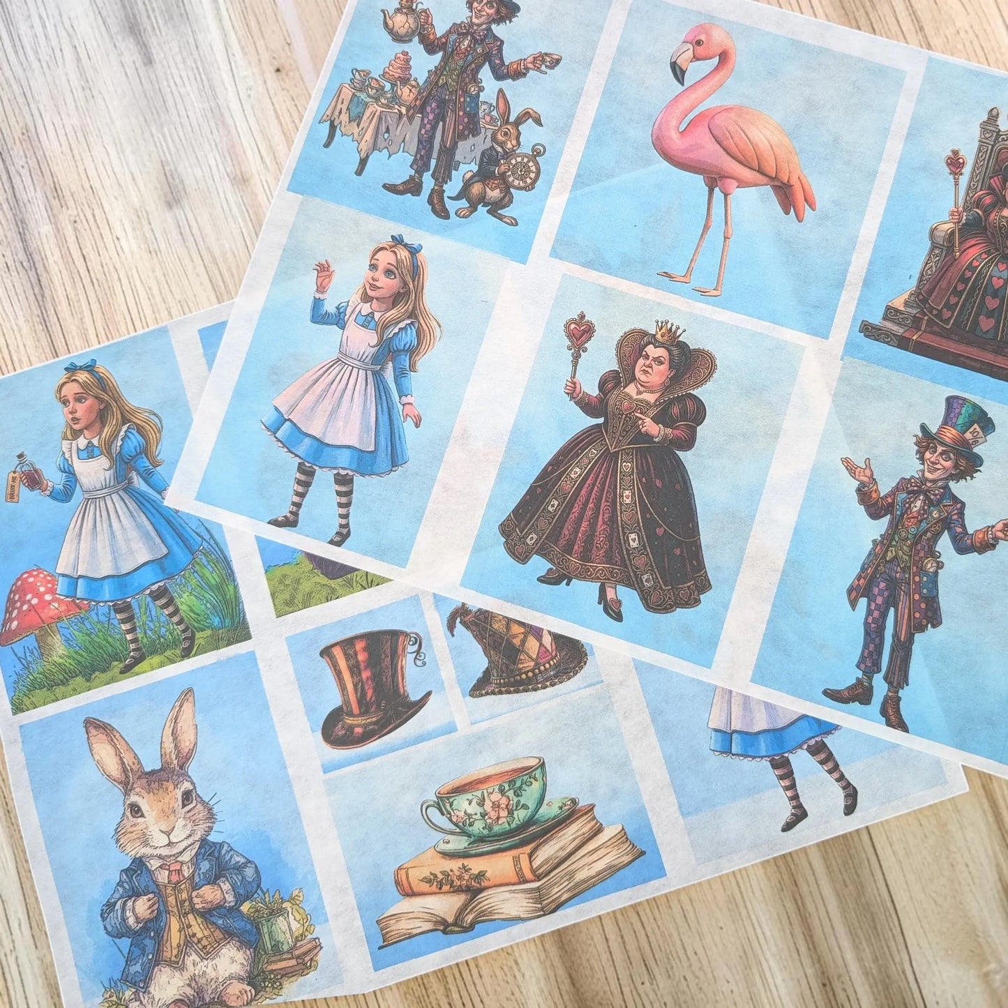 A sheet of decorative paper featuring Alice in Wonderland illustrations, laid out on a light wood surface. The print includes Alice, the Queen, the Mad Hatter, a rabbit, a flamingo, a teacup, books, and hats on a pale blue background.