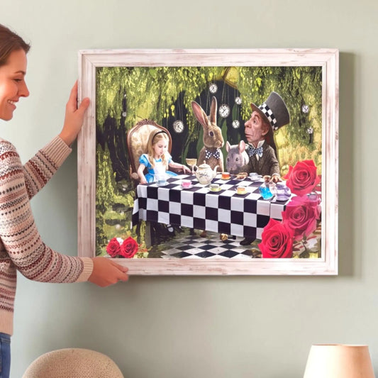 A woman holds a large framed art print depicting a whimsical Alice in Wonderland tea party scene with a checkered tablecloth, roses, and a rabbit, mounted on a light gray wall.