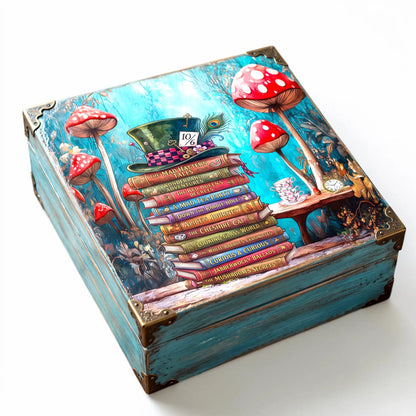 A square decorative box with a whimsical decoupages with a fantasy Alice in wonderland tissue paper, featuring red-and-white mushrooms, a stack of books, a hat, and a turquoise background, photographed on a clean white studio background.
