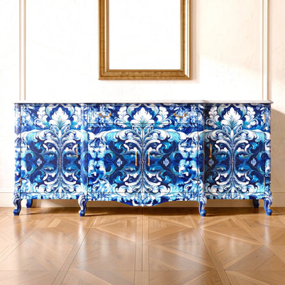 A decorative sideboard or credenza with an ornate blue and white damask-style pattern, shown in a styled interior with a wood parquet floor and a gold-framed mirror on the wall.