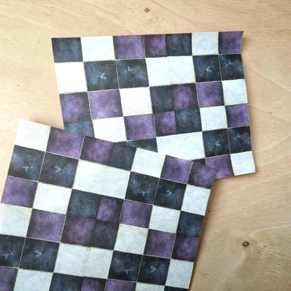 Two square checkered patterned cards or tiles with a purple, black, and off-white checkerboard design, displayed on a light wood surface.