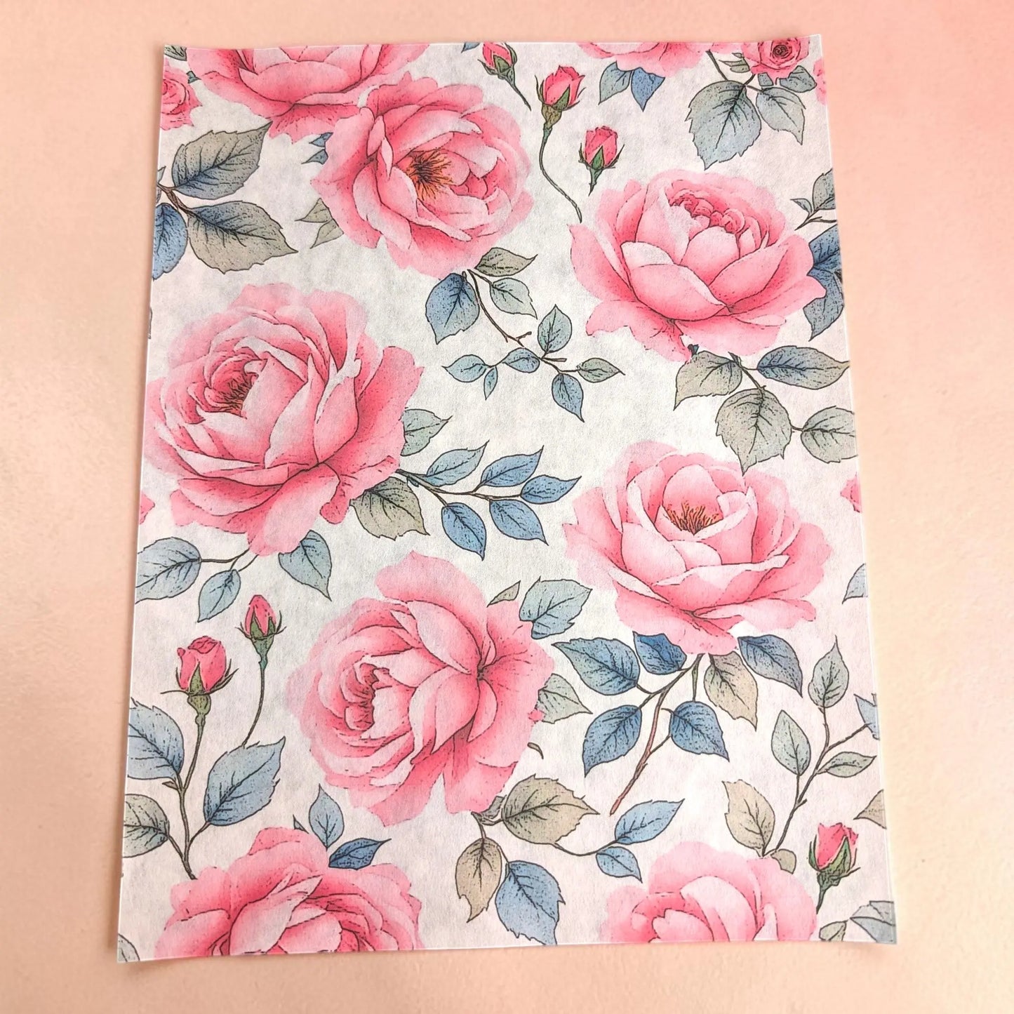 Pink roses tissue paper  with a watercolor-style pink rose pattern on a light background, laid flat on a soft peach-pink surface.
