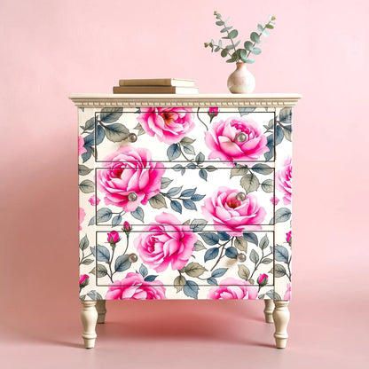 A three-drawer nightstand decoupaged  with a white base and a vibrant pink rose floral print, styled with books and a small vase of eucalyptus against a soft pink background.